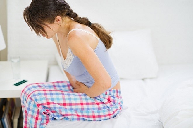 Girl with stomach ache sitting on bed